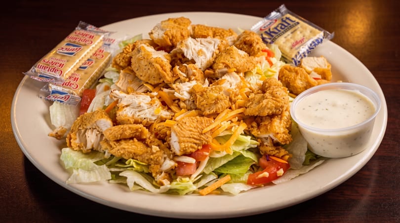 Crispy chicken salad with shredded cheese, tomatoes, and ranch dressing, served with crackers.