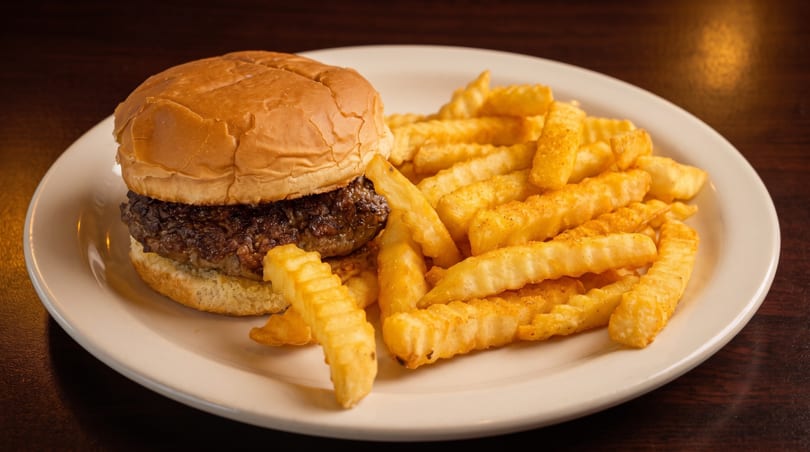 A plain burger with a thick patty and crinkle-cut fries on a white plate.