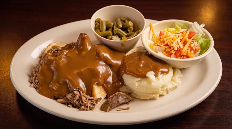 A hot beef sandwich with gravy, mashed potatoes, green beans, and a side salad.