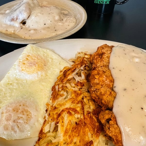 Chicken fried steak with gravy, hash browns, and fried eggs on a white plate.