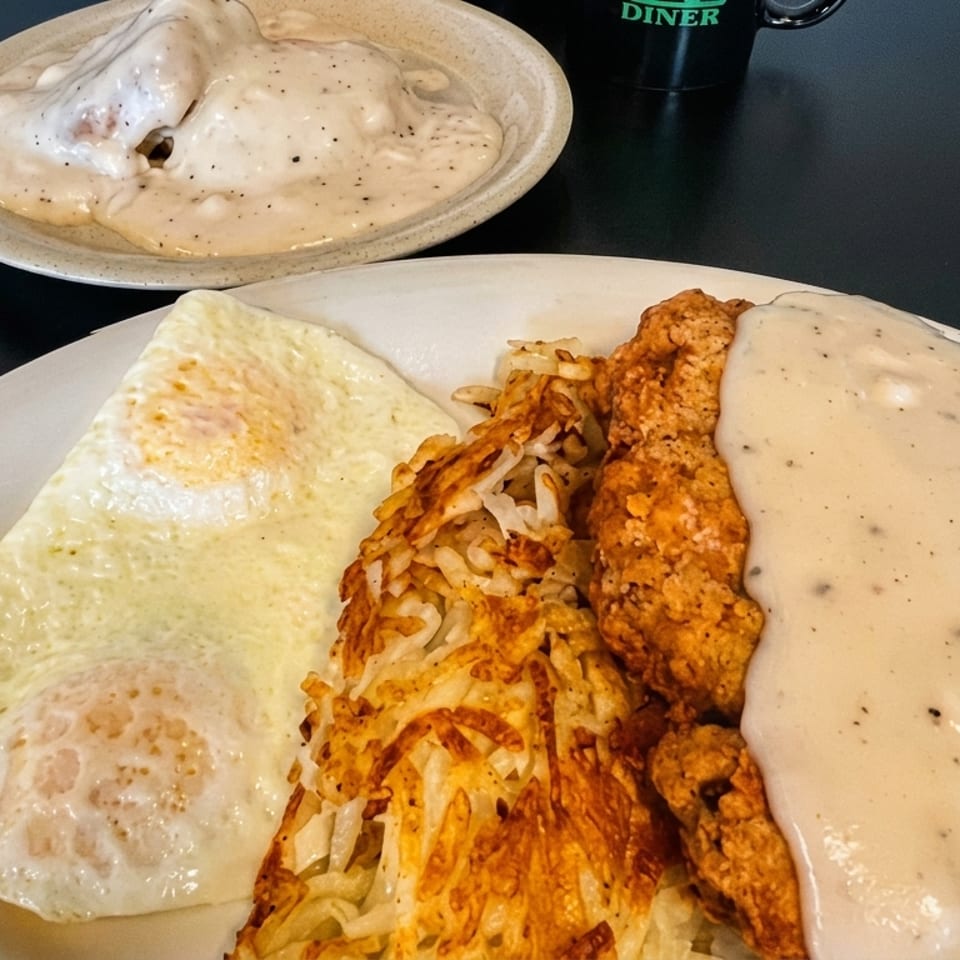 Chicken fried steak with gravy, hash browns, and fried eggs on a white plate.
