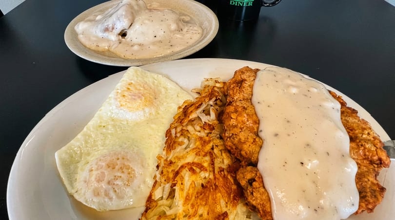 Chicken fried steak with gravy, hash browns, and fried eggs on a white plate.