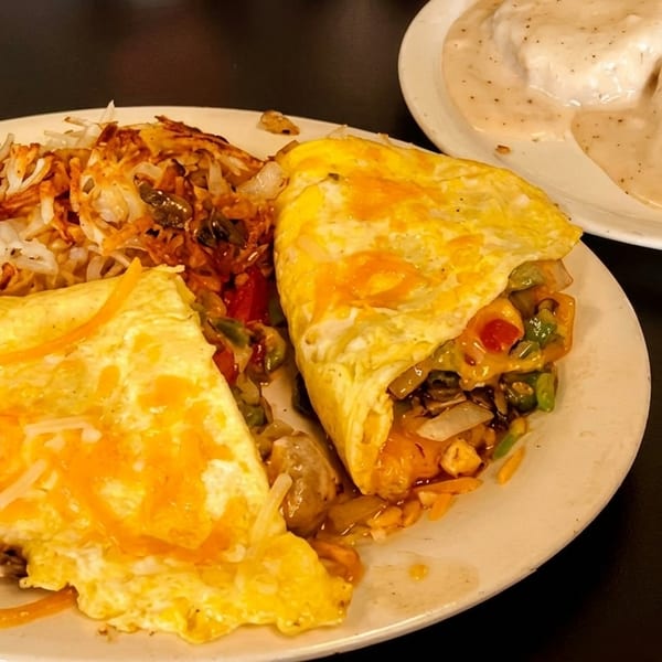 Breakfast plate with two omelets, hash browns, and a side of biscuits and gravy.