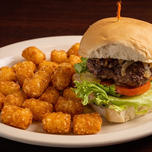 A juicy burger with lettuce, tomato, and caramelized onions, served with a side of crispy tater tots.