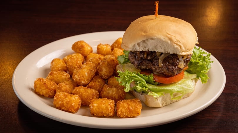 A juicy burger with lettuce, tomato, and caramelized onions, served with a side of crispy tater tots.