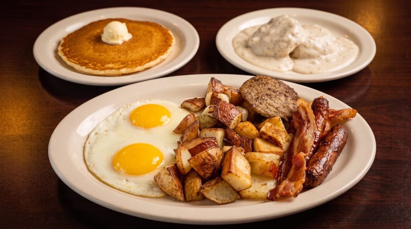A full breakfast spread with pancakes, biscuits and gravy, fried eggs, home fries, bacon, and sausage.