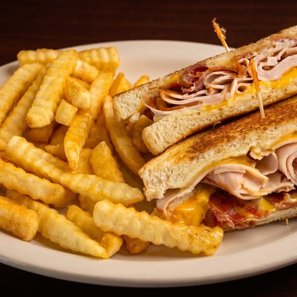 Grilled turkey and bacon sandwich with melted cheese, cut in half, served with crinkle-cut fries.