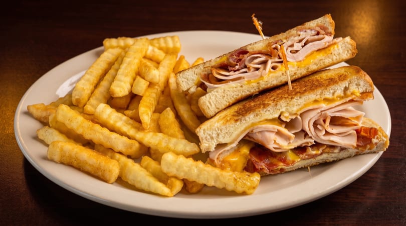 Grilled turkey and bacon sandwich with melted cheese, cut in half, served with crinkle-cut fries.