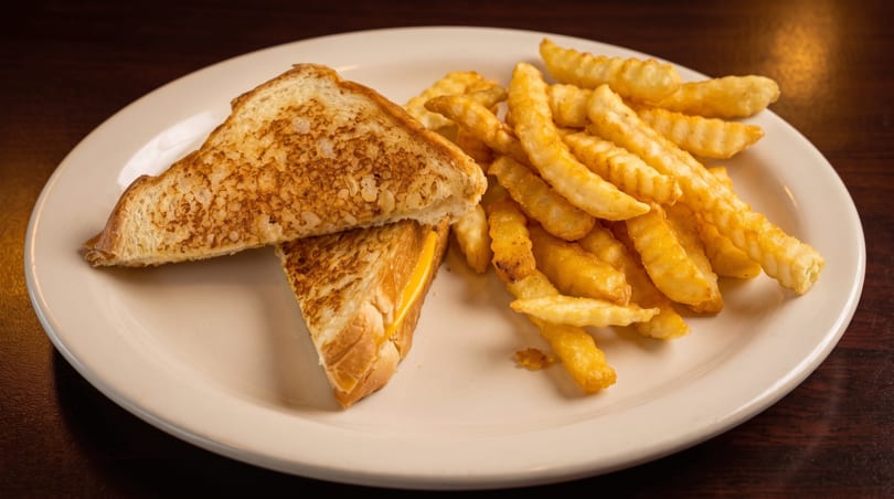 Grilled cheese sandwich cut in half with crinkle-cut fries on a white plate.