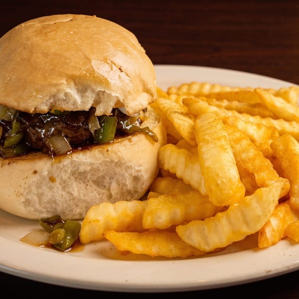 A slider with dark meat, green peppers, and onions, served with crinkle-cut fries on a white plate.